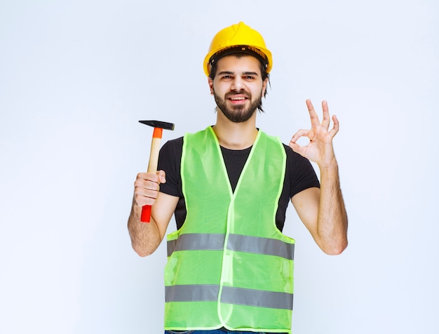 Trabajador de la construcción que sostiene un martillo de garra y que muestra el signo de disfrute.