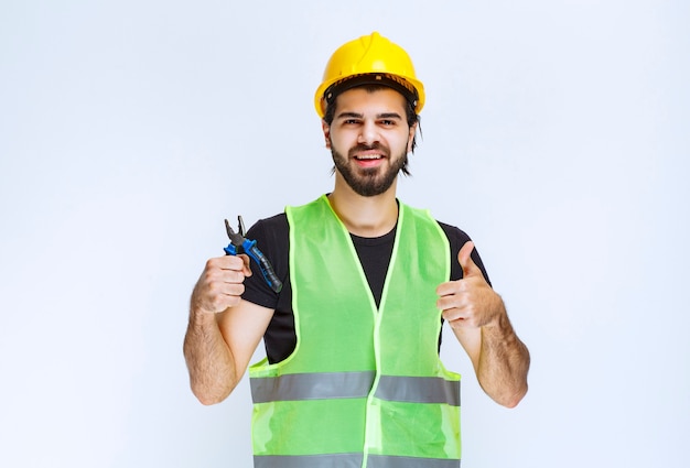 Trabajador de la construcción sosteniendo alicates azules y mostrando el pulgar hacia arriba.