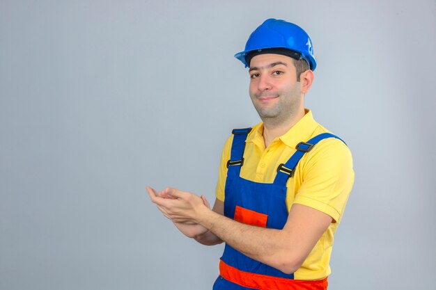 Trabajador de la construcción en uniforme y casco de seguridad azul aplaudiendo con una sonrisa en la cara aislado en blanco