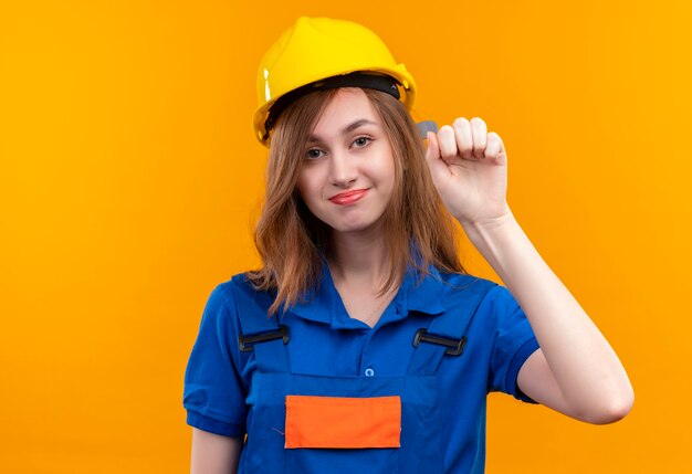 Trabajador constructor joven en uniforme de construcción y golpeando el casco de seguridad