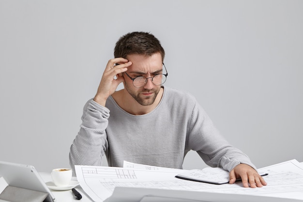 Trabajador creativo masculino inteligente intenta concentrarse en los dibujos, no entiende dónde está su error