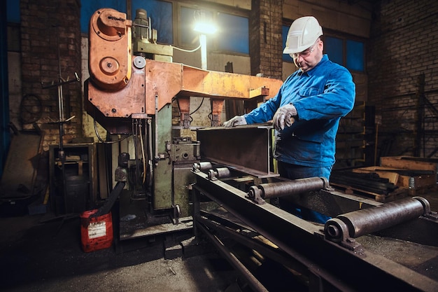 El trabajador está controlando un proceso de corte de rieles en una fábrica metalúrgica muy concurrida.