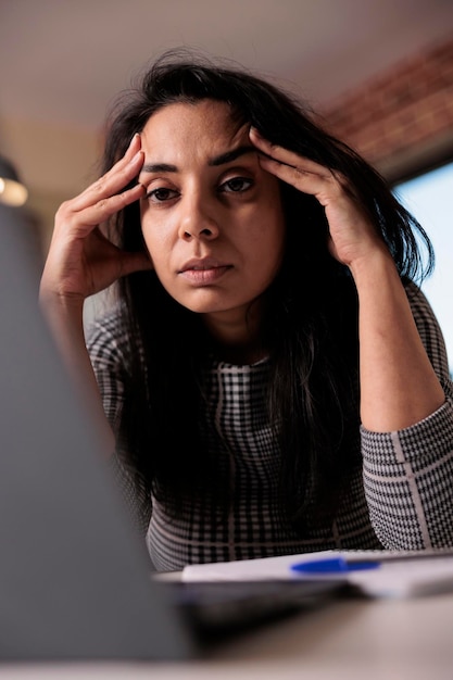 Trabajador exhausto que se siente frustrado por la fecha límite, trabajando desde casa en una laptop. Estar cansado y con sueño, estresado por el trabajo comercial y sentirse sobrecargado de trabajo con dolor de cabeza. Dolor por agotamiento.