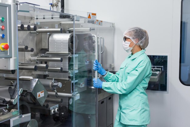Trabajador de una fábrica caucásica con traje de laboratorio azul que trabaja con una máquina con paneles de vidrio