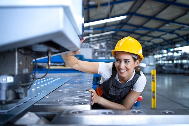Trabajador de fábrica femenina en uniforme protector y casco de máquina industrial operativa en la línea de producción