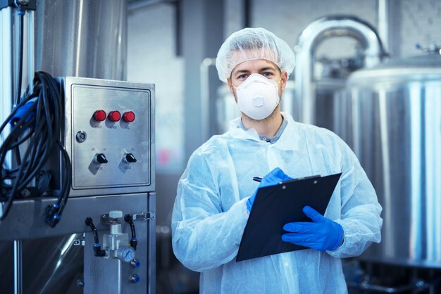 Trabajador de fábrica en uniforme protector blanco con redecilla y máscara de pie por máquina industrial