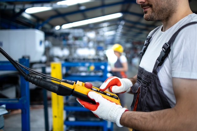 Trabajador de fábrica vistiendo uniforme y casco de máquina industrial operativa con joystick de botón en la sala de producción