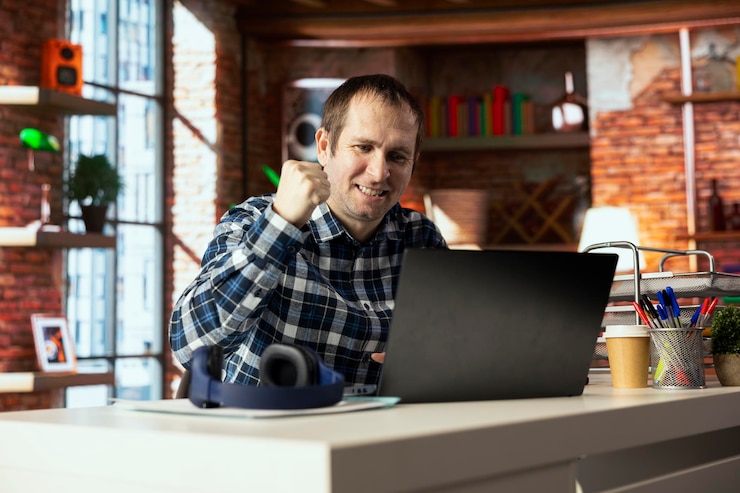 Foto gratuito trabajador feliz en el escritorio sacudiendo el puño para celebrar la finalización de la tarea