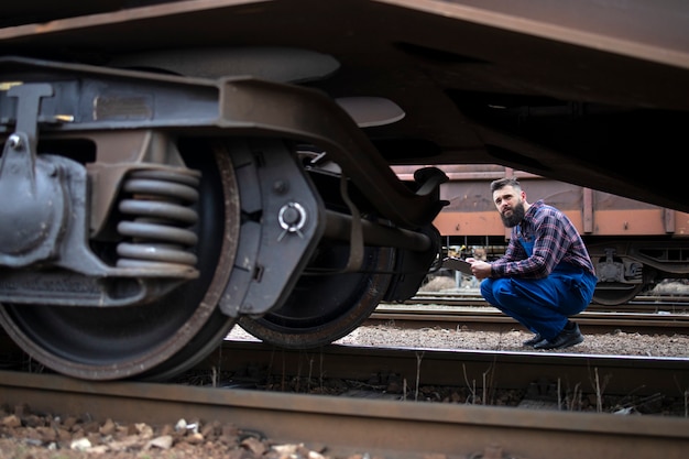 Trabajador de ferrocarril inspeccionando ruedas y frenos del tren de mercancías