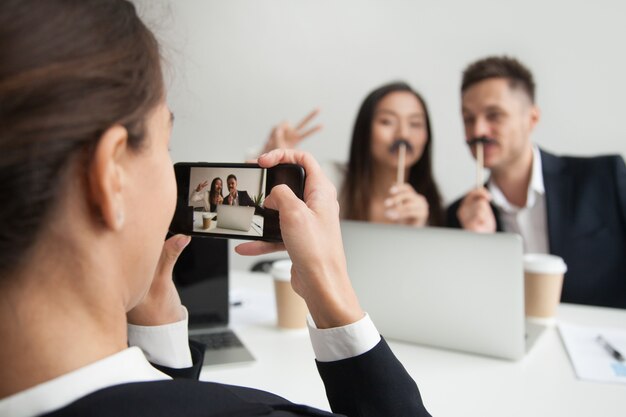 Trabajador haciendo foto de colegas probando accesorio bigote