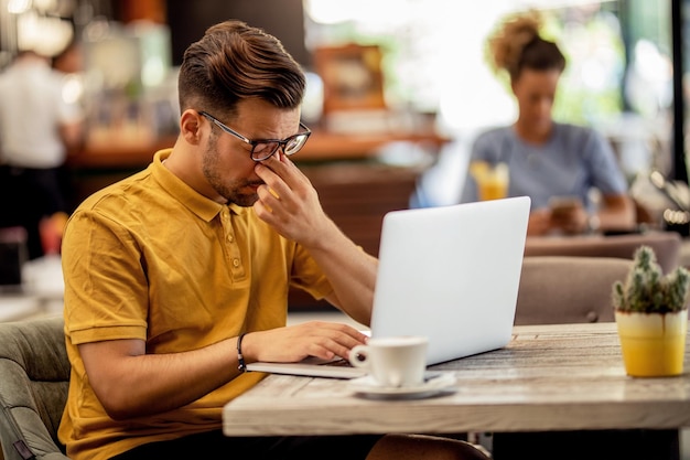 Trabajador independiente cansado que siente dolor mientras trabaja en una computadora en un bar