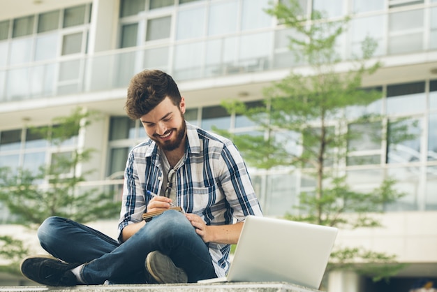 Trabajador independiente lleno de ideas creativas sentado en postura de loto haciendo notas al aire libre