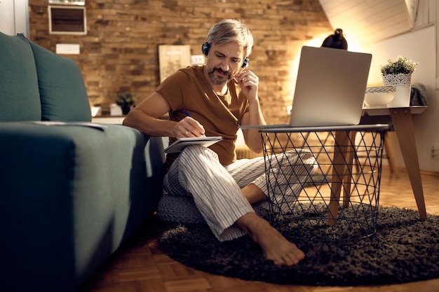 Trabajador independiente en pijama tomando notas durante la conferencia telefónica por la noche en casa