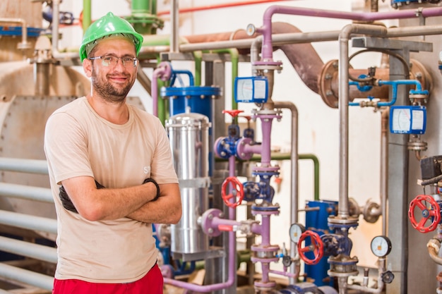 Trabajador de la industria posando dentro de la fábrica con barras y tuberías alrededor