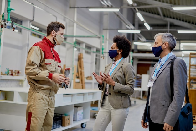 Trabajador industrial hablando con los gerentes de la empresa en las instalaciones de producción durante la pandemia de COVID19