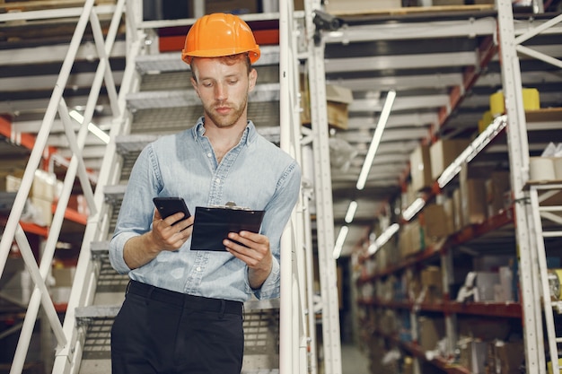 Foto gratuita trabajador industrial en el interior de la fábrica. hombre de negocios con casco naranja. hombre con camisa azul.