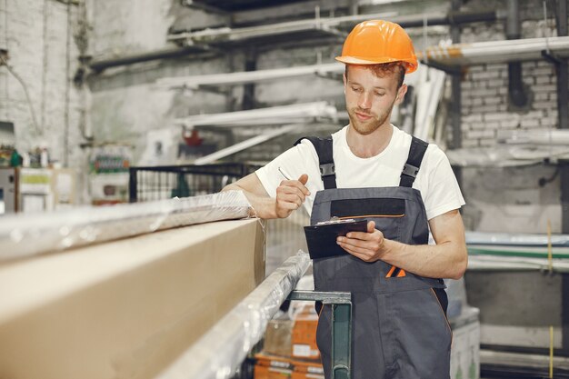 Trabajador industrial en el interior de la fábrica. Joven técnico con casco naranja.