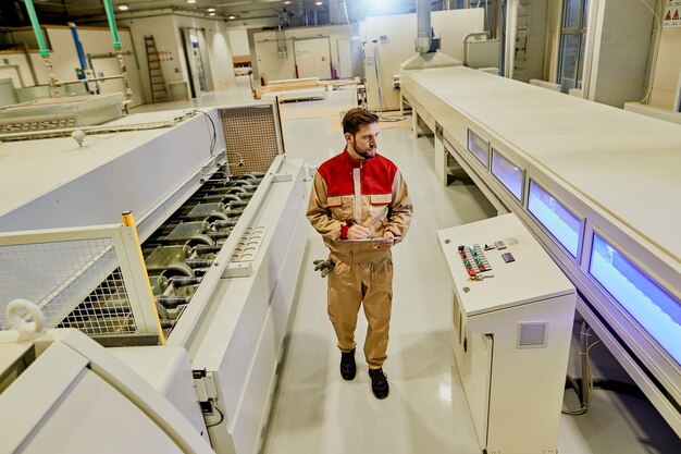 Trabajador industrial supervisando máquinas automatizadas mientras camina por la fábrica de carpintería