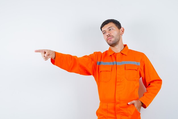 Trabajador joven apuntando hacia afuera en uniforme y mirando positivo.