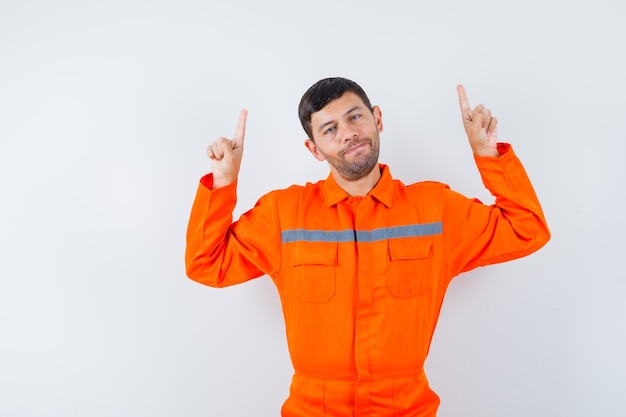 Foto gratuita trabajador joven apuntando con el dedo hacia arriba en uniforme.