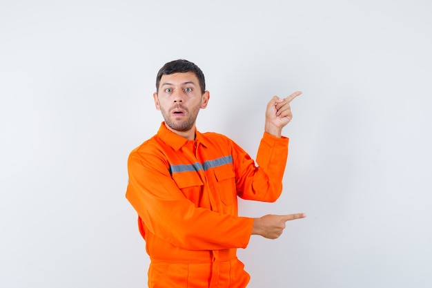 Trabajador joven apuntando hacia un lado en uniforme y mirando perplejo.