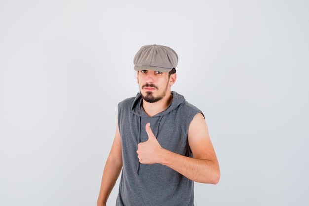 Trabajador joven en camiseta gris y gorra mostrando el pulgar hacia arriba y mirando serio