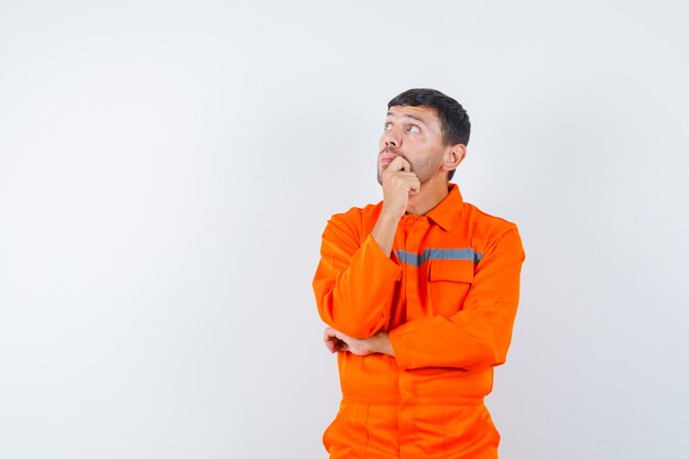 Trabajador joven mirando hacia arriba en uniforme y mirando pensativo.