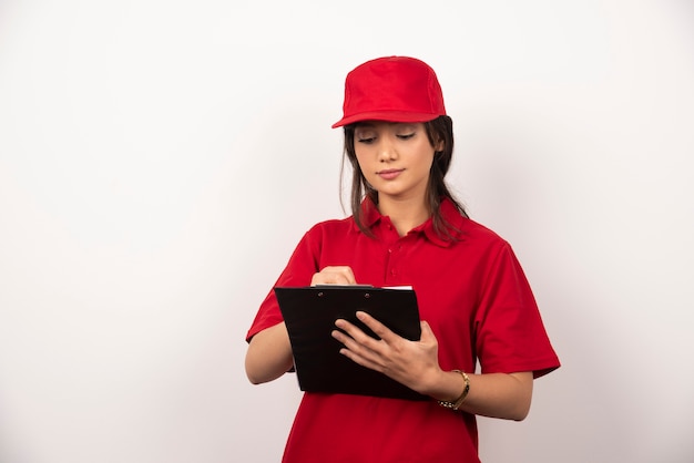 Trabajador joven con uniforme rojo y portapapeles sobre fondo blanco.