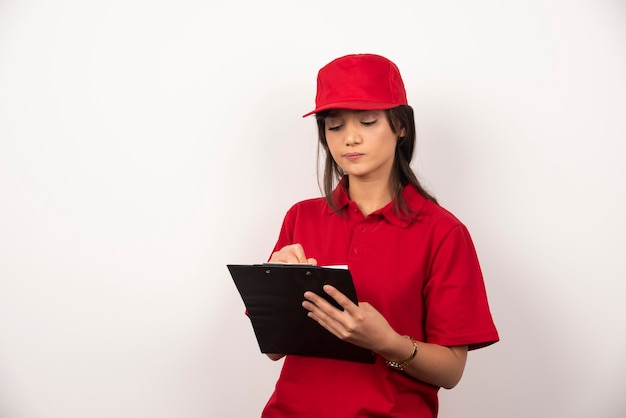 Trabajador joven con uniforme rojo y portapapeles sobre fondo blanco.