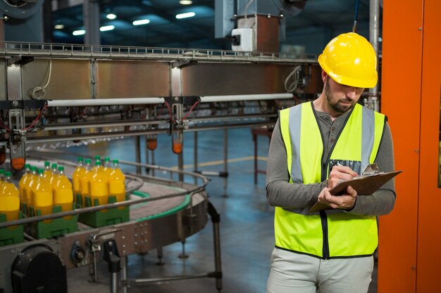 Trabajador masculino escribiendo en el portapapeles en la fábrica de jugos