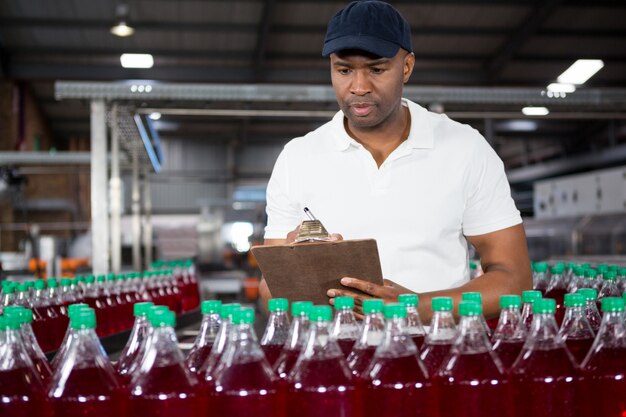 Trabajador masculino escribiendo en el portapapeles en la fábrica.