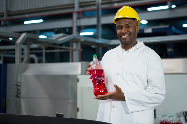 Trabajador masculino mostrando botella de jugo en la fábrica.