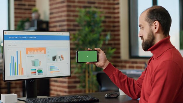 Trabajador masculino sosteniendo un teléfono inteligente con pantalla verde horizontal en la oficina de negocios. Adulto joven que trabaja con clave de croma en blanco y plantilla aislada con fondo de maqueta en la pantalla del teléfono móvil.