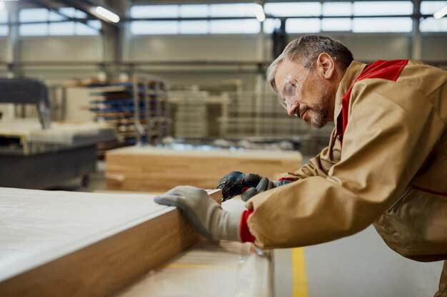 Trabajador masculino usando un taladro mientras fabrica muebles en un taller de carpintería