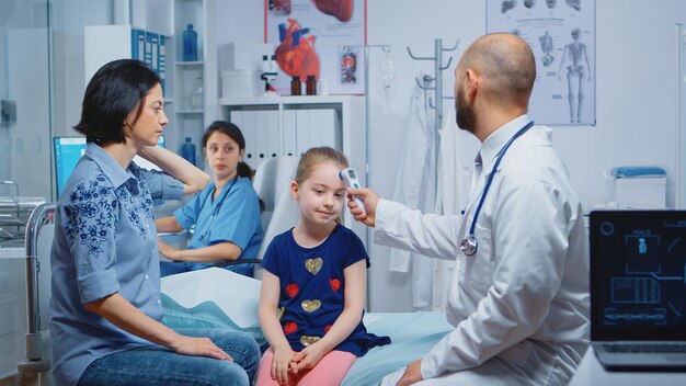 Trabajador médico tomando la temperatura de la niña con termómetro durante la consulta. Médico profesional de la salud especialista en medicina que brinda servicios de atención médica, tratamiento de consulta en el hospital