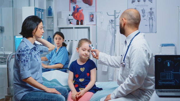 Trabajador médico tomando la temperatura de la niña con termómetro durante la consulta. Médico profesional de la salud especialista en medicina que brinda servicios de atención médica, tratamiento de consulta en el hospital