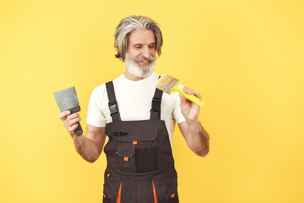 Trabajador en mono. Hombre con herramientas. Senior con espátula.