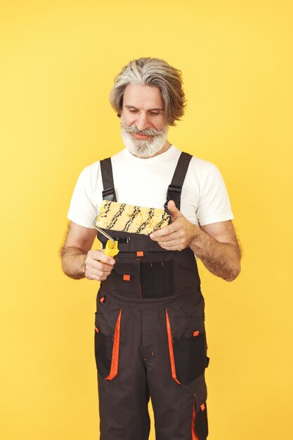 Trabajador en mono. Hombre con herramientas. Senior con rodillo de pintura.
