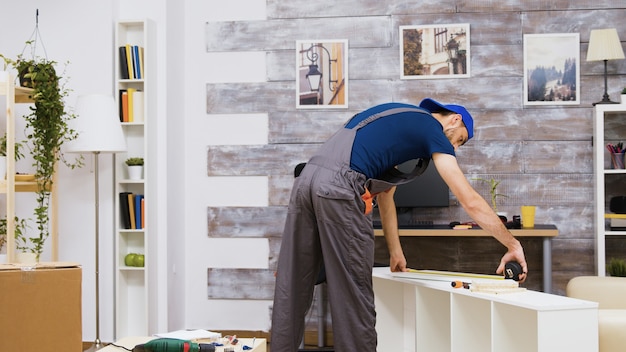 Trabajador de montaje de muebles de pie con instrucciones de lectura y usando una cinta métrica. Herramientas de trabajador.