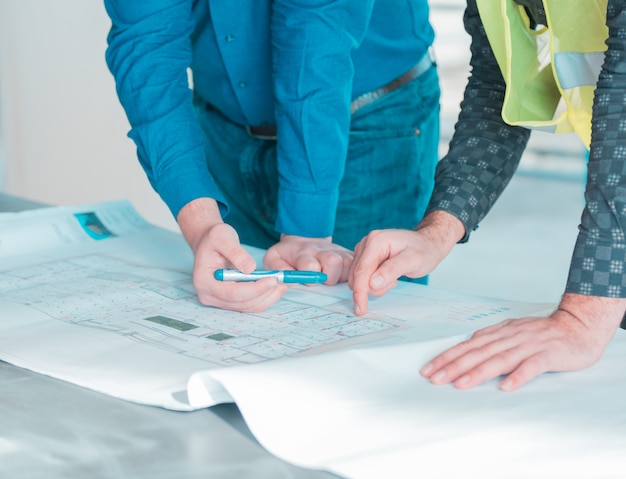 Un trabajador muestra detalles importantes en el plan arquitectónico de un proyecto a otro.
