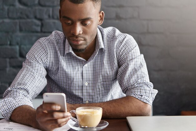 Trabajador de oficina africano guapo vistiendo camisa a cuadros con mangas enrolladas disfrutando de la comunicación en línea