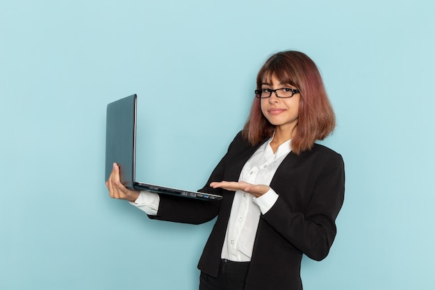 Trabajador de oficina femenino de vista frontal sosteniendo portátil y sonriendo sobre la superficie azul