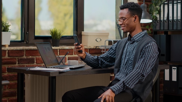 Trabajador de oficina que usa un teléfono inteligente para hablar en una videollamada en el trabajo, reuniéndose en una videoconferencia en línea con colegas. Consultor chateando en una llamada remota de teletrabajo, usando un teléfono móvil.