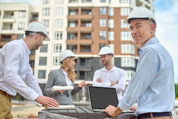 Trabajador de pie entre sus tres compañeros de trabajo en el sitio de construcción