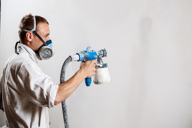 Foto gratuita trabajador pintando la pared con pistola en color blanco.