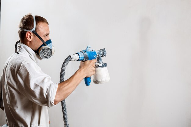 Trabajador pintando la pared con pistola en color blanco.