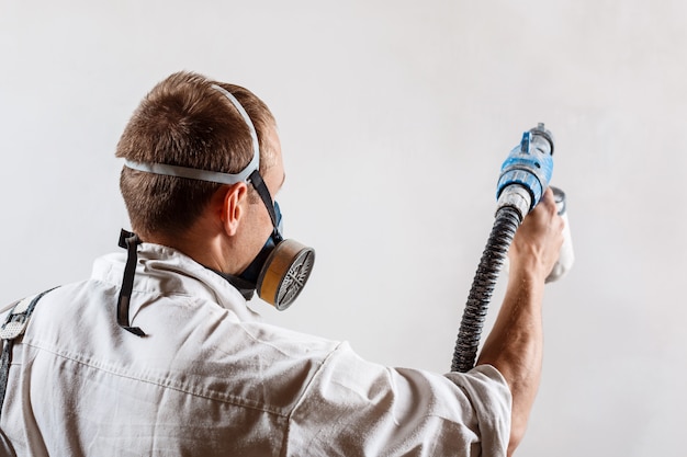 Foto gratuita trabajador pintando la pared con pistola en color blanco.