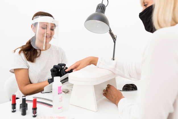 Trabajador con protector facial en el salón de uñas