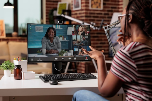 Trabajador remoto hablando con el equipo en videollamada, sesión informativa en línea, comunicación por videoconferencia, concepto de teletrabajo. Mujer charlando en una reunión virtual, concéntrese en la pantalla de la computadora, vista posterior