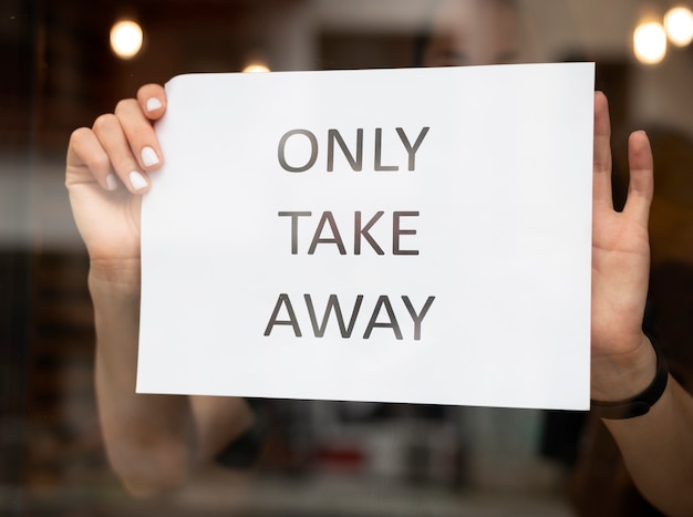 Trabajador de restaurante poniendo un cartel de comida para llevar en frente del restaurante